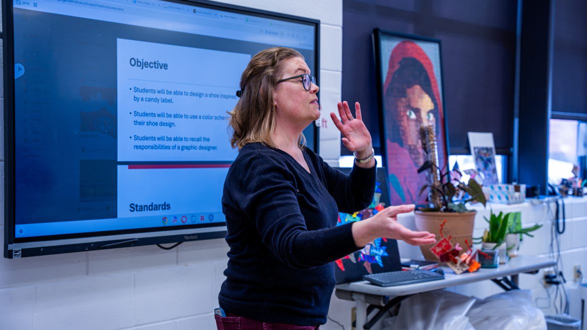 teacher giving instruction in front of a digital screen